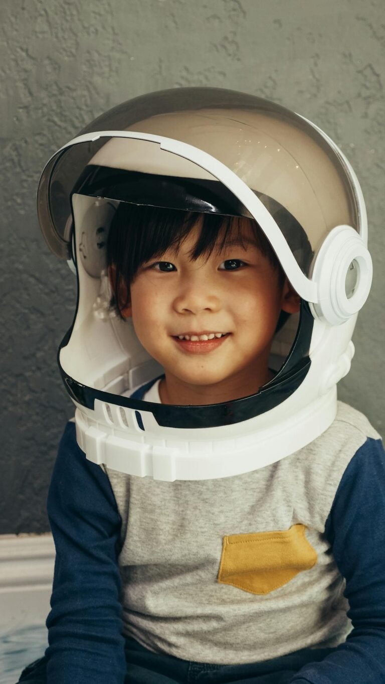 A smiling young boy wearing a toy astronaut helmet, embodying childhood imagination and play indoors.